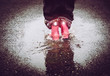 Girl having fun, jumping in water puddle on wet street, wearing rain boots with reflective detail fabric stripes shining. High visibility and safety in dark concept.