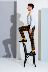 Wall Mural - side view of man in plaid trousers standing on chair on white and grey