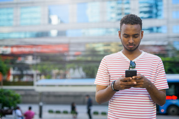 Wall Mural - Young handsome African bearded man using phone in the city