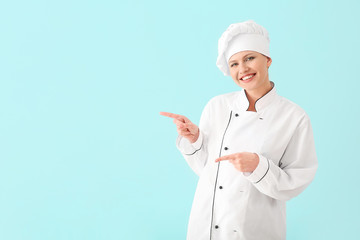 Canvas Print - Beautiful female chef pointing at something on light background