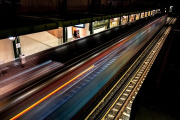 Fast driving metro train at night with light trails in Athens, Greece with a platform and railway