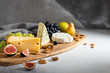 Cheese plate served with camembert, brie, blue cheese, maasdam, grapes, pear, figs and nuts on a wooden board on gray background. Side view. Copy space. Dairy products, keto diet