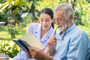 senior elderly man reading book with nurse during breakfast in garden at nursing home