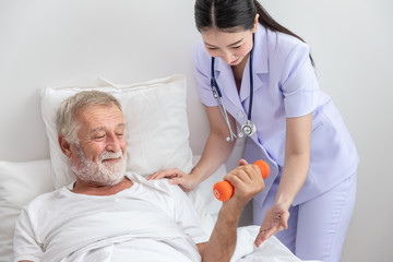 Senior man holding dumbbells with physiotherapist in bedroom at nursing home