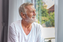 Senior Elderly Man Standing And Looking Out Of Window In Bedroom After Waking Up In Morning