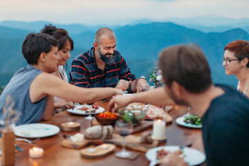 Wall Mural - Friends and family gathered for picnic dinner for Thanksgiving. Festive young people celebrating life with red wine, grapes, cheese platter, and a selection of cold meats