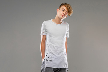 handsome emotional teenager boy posing in studio against gray, young man in a light t-shirt, mockup