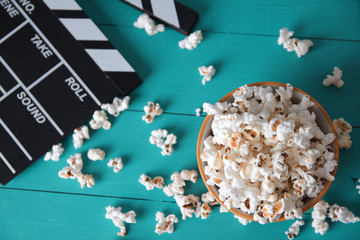 a plate of popcorn on a blue wooden background, top view, next to a flapper numerator for movies