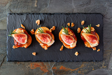 Poster - Crostini appetizers with figs, brie cheese and walnuts. Above view on a slate serving platter.