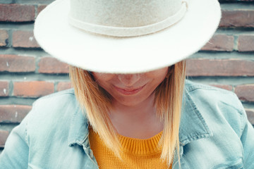 close up portrait of a smiling young caucasian blond woman with a half-covered face by a white hat