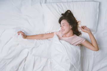 Young woman sleeping well in bed hugging soft white pillow. Teenage girl resting. good night sleep concept. Girl wearing a pajama sleep on a bed in a white room in the morning. warm tone.