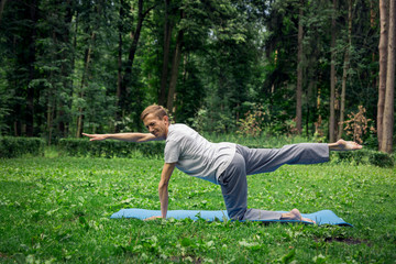 Young handsome  man in sportswear does stretching in the park on the green grass. Prepare a warm-up for yoga or fitness classes