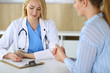 © Iryna - Woman doctor and patient sitting and talking at medical examination in hospital or clinic. Blonde therapist cheerfully smiling. Medicine and healthcare concept