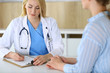 © Iryna - Woman doctor and patient sitting and talking at medical examination in hospital or clinic. Blonde therapist cheerfully smiling. Medicine and healthcare concept