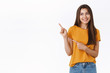 © Cookie Studio - Cheerful, carefree happy young friendly woman in yellow t-shirt, smiling laughing joyfully as looking enthusiastic upper left corner, pointing with fingers at someone or promo, white background