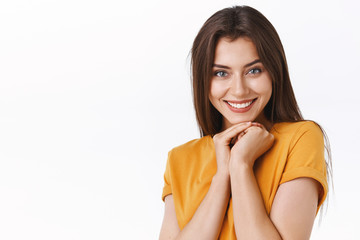 Coquettish attractive happy girlfriend receive charming expensive gift, smiling joyfully, receive desired thing, clasp hands near jawline in flirty feminine pose, standing white background