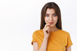 Pensive good-looking daring young modern woman in yellow t-shirt smiling sassy and creative, touching lip have interesting idea, intrigued with promo, standing white background thinking