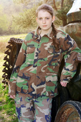 Girl in military uniform with camouflage spots posing in front of a tank