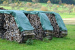 stacks of firewood drying on meadow covered with plastic tarps