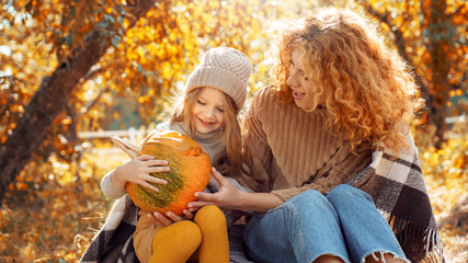 Mother and daughter wrapped in plaid holding halloween pumpkin