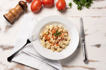 Italian tortellini (capeletti, agnolini) with tomato sauce in a white plate on rustic white wooden table background