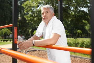 Wall Mural - Handsome mature man with bottle of water on sports ground. Healthy lifestyle