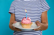 Happy boy holding birthday cupcake with candle on blue background, closeup