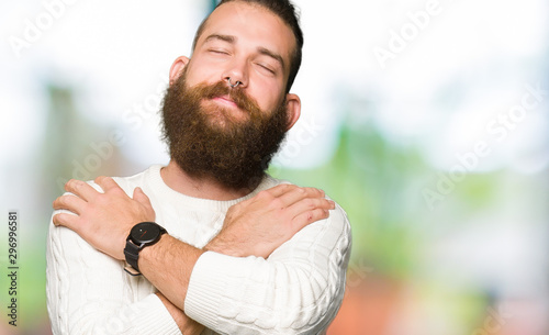 Cuadros en Lienzo Young hipster man wearing winter sweater Hugging oneself happy and positive, smiling confident