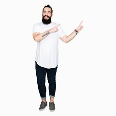 Wall Mural - Young hipster man with long hair and beard wearing casual white t-shirt smiling and looking at the camera pointing with two hands and fingers to the side.