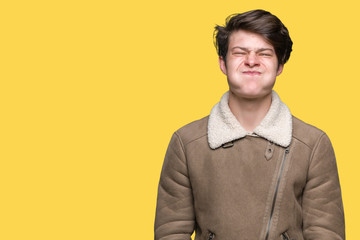 Young handsome man wearing winter coat over isolated background puffing cheeks with funny face. Mouth inflated with air, crazy expression.