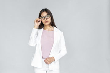 Wall Mural - Confident serious smart young adult indian business lady in formal wear suit standing isolated on grey background with copy space. Successful woman looking at camera through eyewear