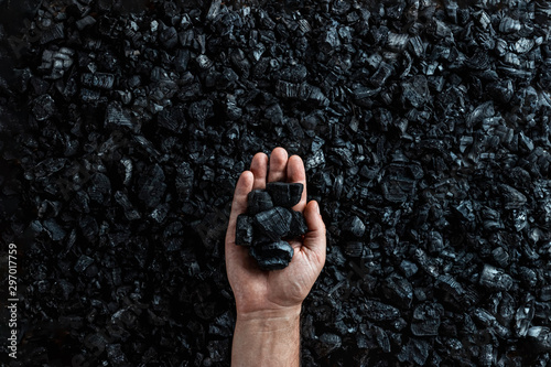 Fotografía Male hand with coal on the background of a heap of coal, coal mining in an open pit quarry, copy space