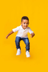 Adorable afro baby boy jumping over yellow studio background