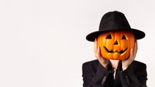 Man In Black Suit Holding Pumpkin Head In Hands On White