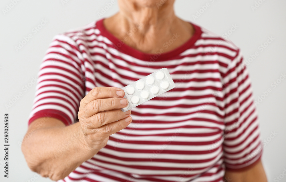 Elderly woman with pills on light background