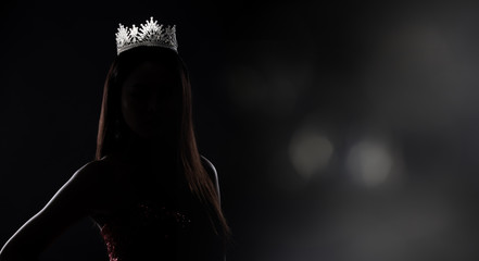 Portrait of Miss Pageant Beauty Contest in sequin Evening Ball Gown long dress with sparkle light Diamond Crown, silhouette low key exposure with curtain, studio lighting dark background dramatic