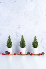 Poster - Three christmas tree with pine cone and decor xmas ball on white table and marble tile wall background.clean minimal simple style.holiday still life mockup banner with space to adding text