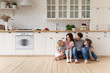 © fizkes - Happy family with children sitting on floor in modern kitchen