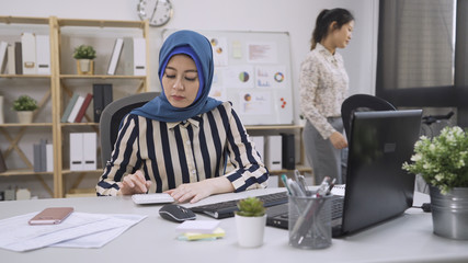 Wall Mural - beautiful islam woman accountant working with computer and counting calculator. elegant asian chinese coworker walking back to seat in modern office. diverse young people worker employee workplace.