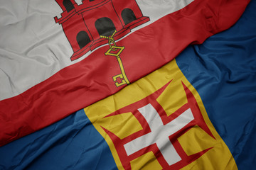 waving colorful flag of madeira and national flag of gibraltar.