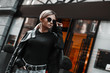 canvas print picture - Fashion stylish woman in leather jacket, jeans, sweater and sunglasses walking on road on shops background. Elegant trendy outdoors portrait of pretty girl model on city street