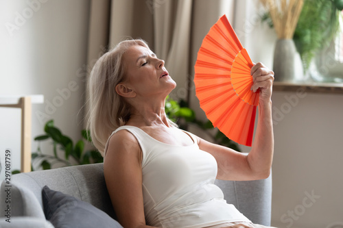Photographie Stressed old woman waving fan suffer from overheating at home