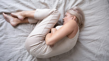 Depressed Mature Woman Lying Alone On Bed In Fetal Position