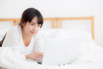 Wall Mural - Beautiful portrait asian young woman smile lying on bed using laptop computer with happy at bedroom for leisure and relax, freelance with girl working notebook, communication concept.