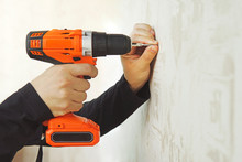 Concept. Worker Is Screwing The Drywall Screw By Screw Gun To The Plasterboard Wall In Apartment Is Under Construction, Remodeling, Renovation, Overhaul, Extension, Restoration And Reconstruction
