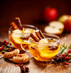 Wall Mural - Mulled cider with apple slices, cinnamon sticks, cloves, anise stars and citrus fruits in glass cups on a wooden rustic table. Delicious, traditional hot drink