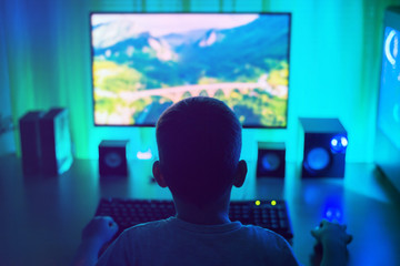 Poster - Boy work on computer. Dark scene with lots of light. View from back, third person. Concept of a young hacker.
