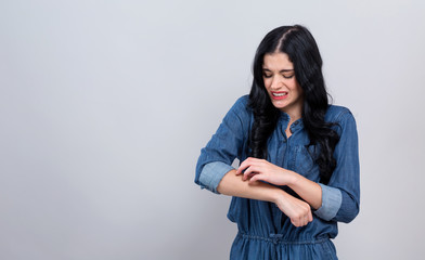 Young woman scratching her itchy arm. Skin problem. on a gray background