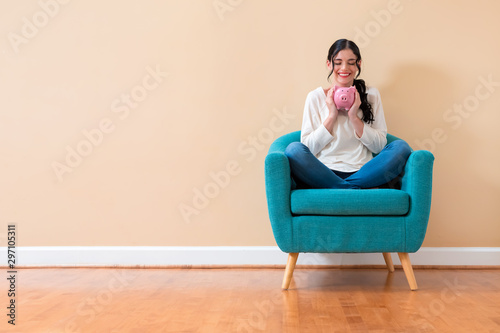 Fotomural Young woman with a piggy bank sitting in a chair