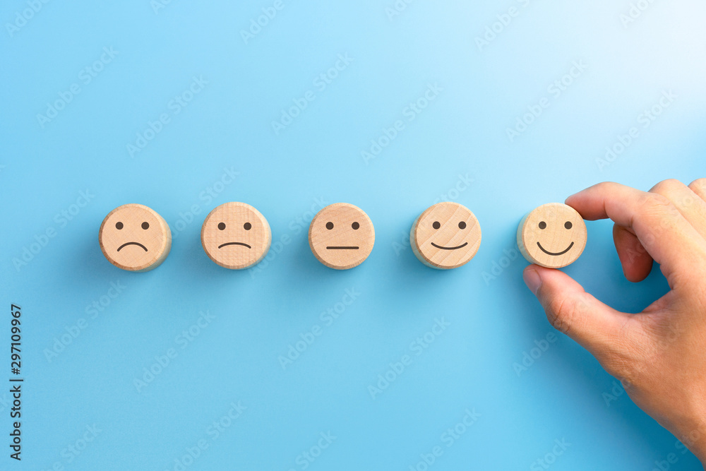 Customer service evaluation and satisfaction survey concepts. The client's hand picked the happy face smile face icon on wooden cube on blue background. copy space - obrazy, fototapety, plakaty 